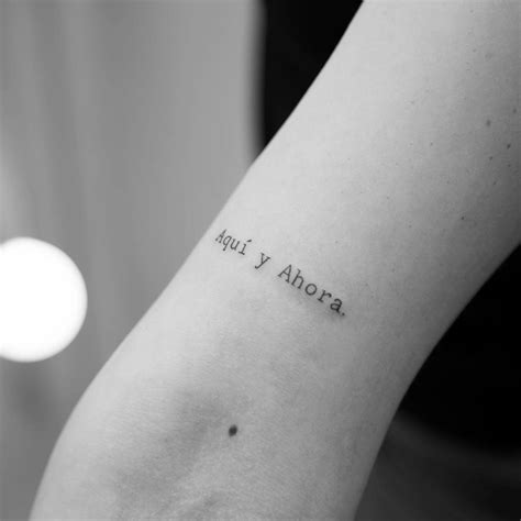 "Aquí y ahora" lettering tattoo located on the bicep.