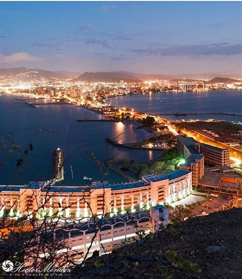 an aerial view of a city at night with lights on the buildings and water in the background