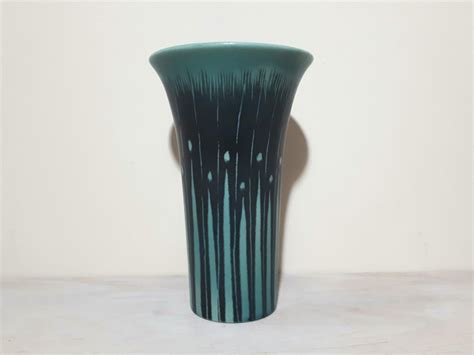 a green and black vase sitting on top of a white table next to a wall
