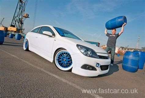 a white car with blue rims is parked in front of a man holding two barrels