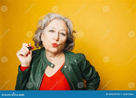 Senior Woman Applying Red Lipstick Over a Yellow Background Stock Photo ...