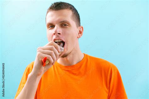 An angry man eating a milk chocolate bar is packaged in the plastic paper on blue background ...
