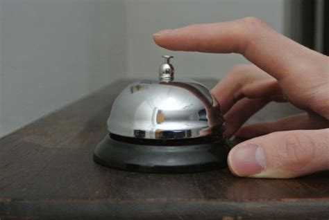 a close up of a person's hand near a silver bell on a wooden table