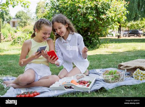 Girl sharing mobile phone with sister sitting at park Stock Photo - Alamy
