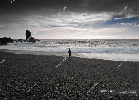 Man walking along black beach, djupalonssandur, snaefellsnes, iceland ...