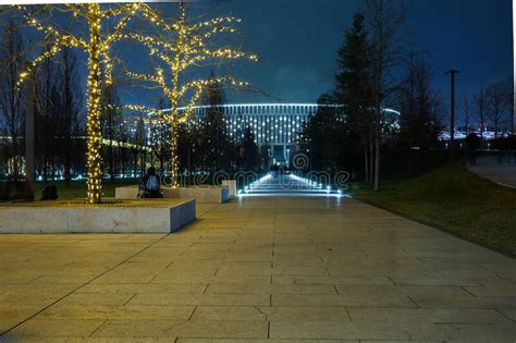 Night Winter Park with Hiking Trails Illuminated by Bright Spotlights on the Lawn and Trees in ...