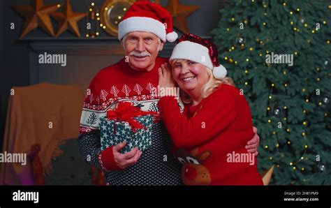 Senior wife and husband looking at camera near glowing Christmas tree, waving hello, making a ...