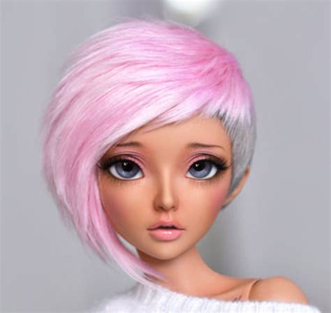 a doll with pink hair and blue eyes wearing a white sweater, posing for the camera