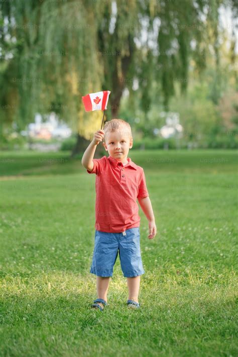 Caucasian child boy holding waving Canadian flag outdoor. Kid child citizen celebrating Canada ...