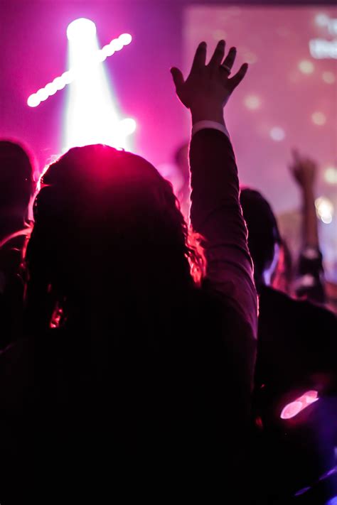 a person raising their hands up in the air at a concert with lights on behind them