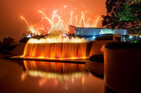 fireworks are lit up in the sky above a water fountain with orange and ...