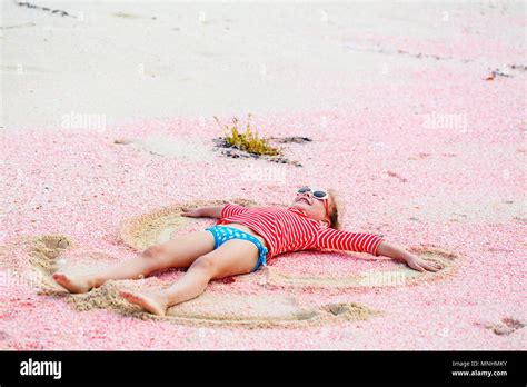 Little girl making sand angel on beautiful pink sand beach at tropical ...