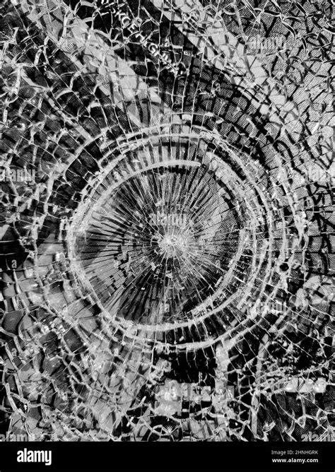 Broken glass. Round hole with radial cracks in the glass. Round white cracks in glass on black ...