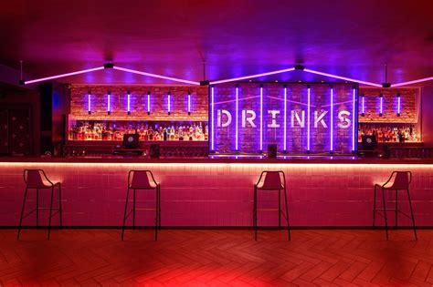 the bar is lit up with purple lights and barstools in front of it