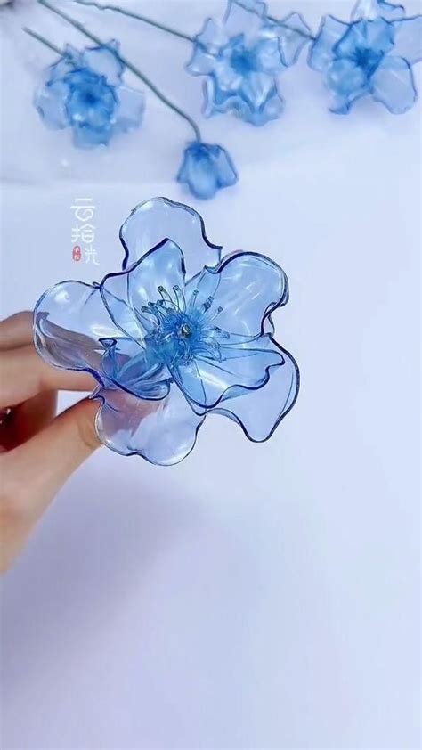 a hand holding a blue flower on top of a white table