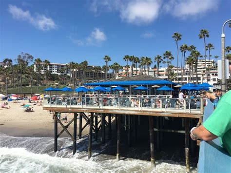 people are standing on the pier near the beach with blue umbrellas and ...