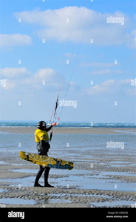 Kitesurfer-with board and kite returning after kitesurfing on West Wittering's beach at low tide ...