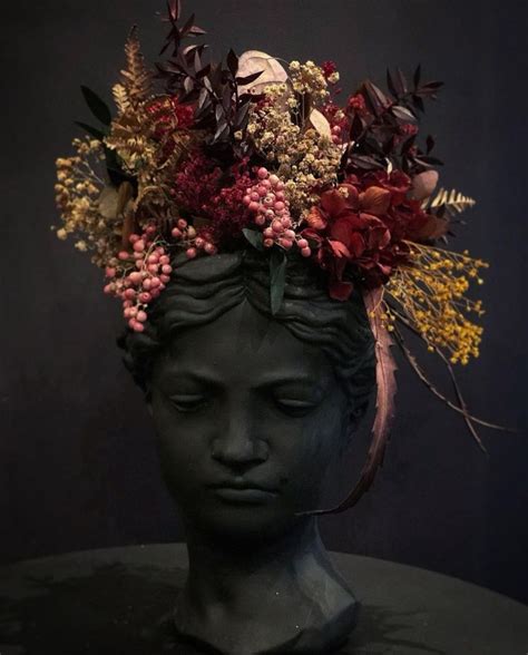 a head with flowers in it sitting on top of a black table next to a dark wall
