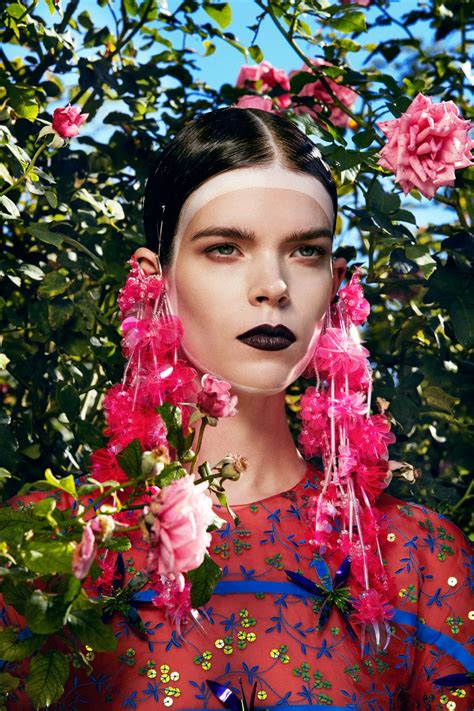 a woman with flowers in her hair and black lipstick on her face, surrounded by pink flowers