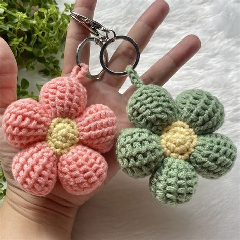 two crocheted flower keychains being held by a person's hand