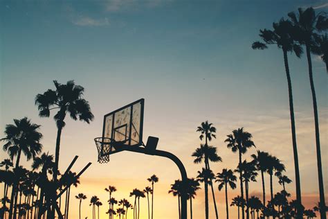 a yellow and blue sunset in venice los angeles forming silhouettes of a basketball court and ...