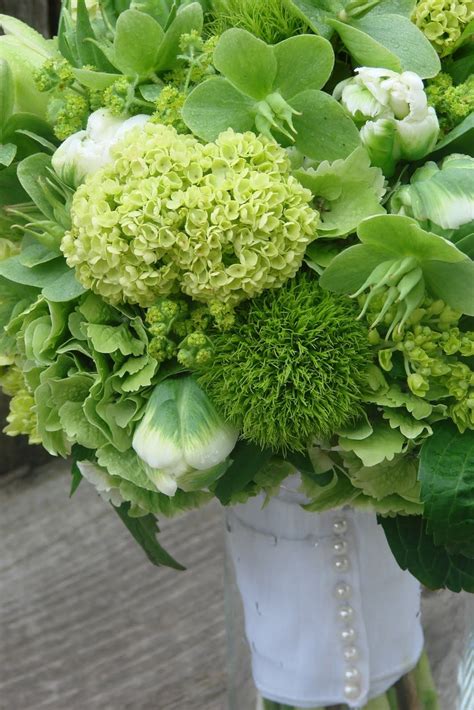 a bouquet of green flowers and greenery in a vase on a wooden table outside