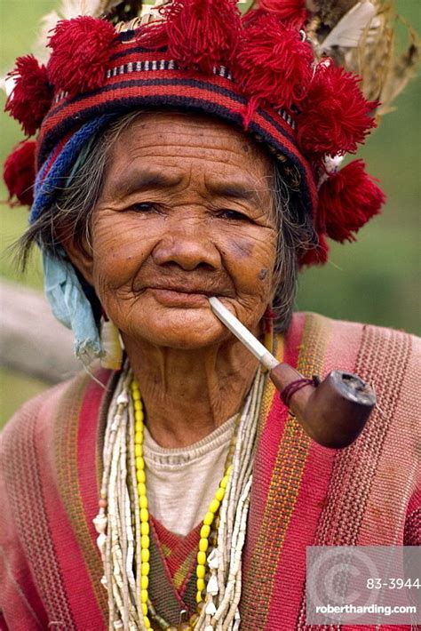 Portrait of an elderly woman of the Ifugao tribe wearing a woven hat decorated with feathers and ...