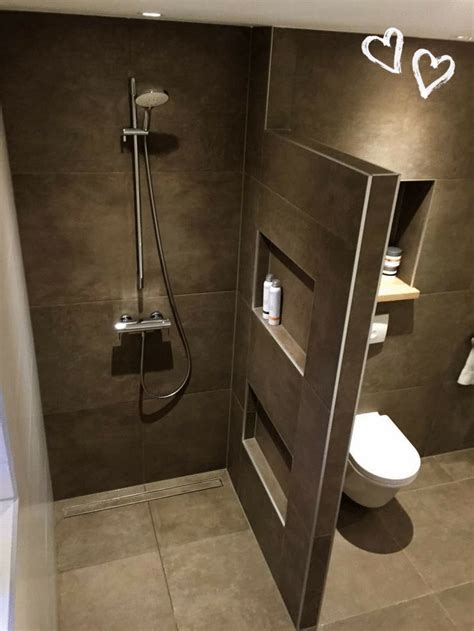 a bathroom with a walk in shower next to a white toilet and brown tiled ...