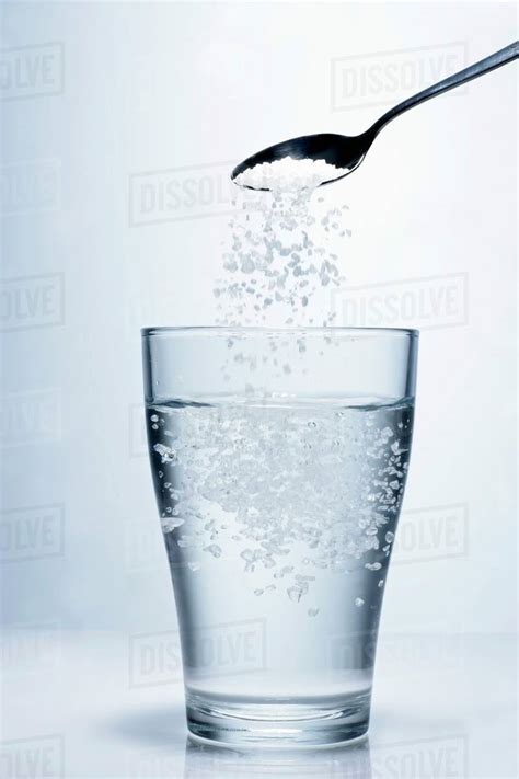 Sprinkling salt into a glass of water - Stock Photo - Dissolve