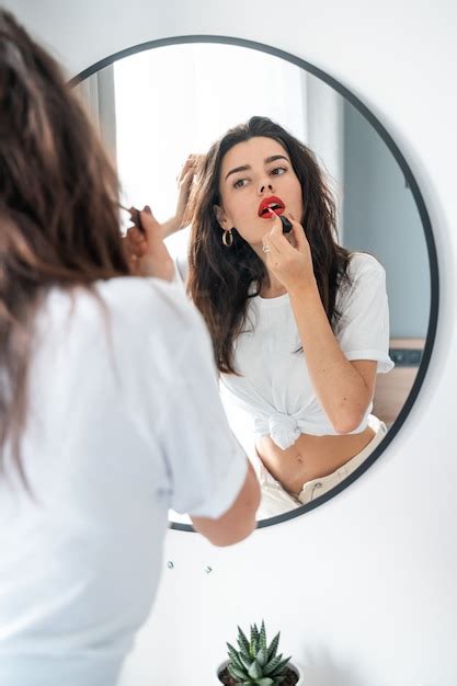 Free Photo | Young woman applying lipstick looking at mirror