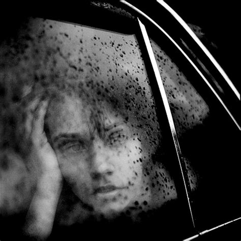 black and white photo of woman looking out car window with rain drops on her face