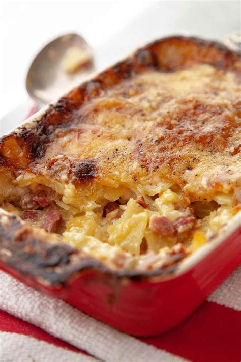 A red dish filled with a layered ham, cheese, and potato casserole on a ...