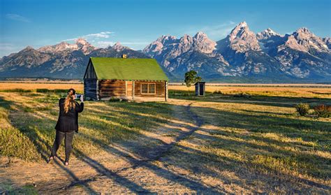 a woman standing in front of a small cabin with mountains in the backgroud