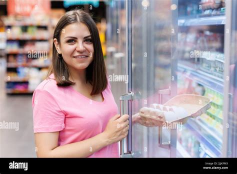 Young woman shopper in the grocery store choosing fresh chicken eggs. A beautiful smiling woman ...