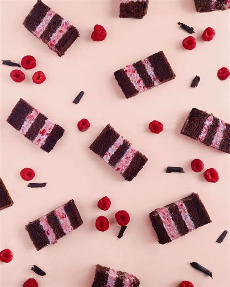several pieces of chocolate cake with raspberries and cherries scattered around them on a pink ...