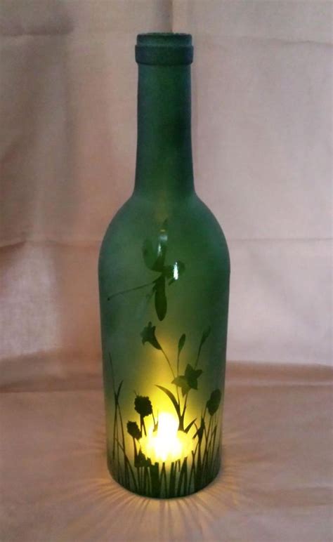 a green glass bottle with flowers on it sitting on a white tablecloth covered surface