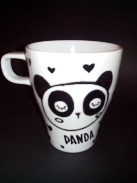 a white coffee cup with black and white panda on it's side, sitting on a table