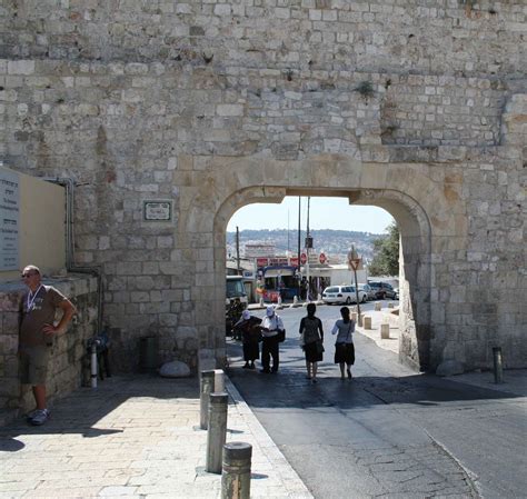 people are walking through an arch in the stone wall that leads to a parking lot