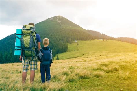 Premium Photo | Father and son with backpacks hiking together in summer mountains. back view of ...