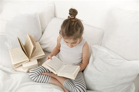 Cute little girl reading a book on the bed in the bedroom. | Free Photo