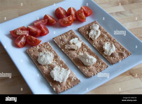 Simple snack of ak-mak crackers, humus, and sliced cherry tomatoes on a ...