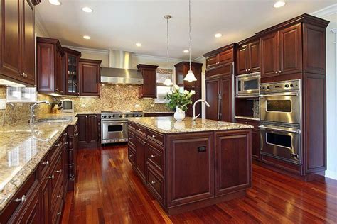 Kitchen in luxury home with dark cherry wood cabinetry, wood flooring, and granite island ...