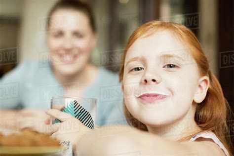 Girl with a milk moustache at dining room table - Stock Photo - Dissolve