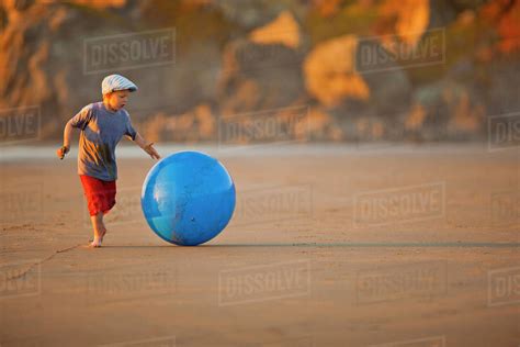 Young boy rolling a swiss ball along a beach. - Stock Photo - Dissolve