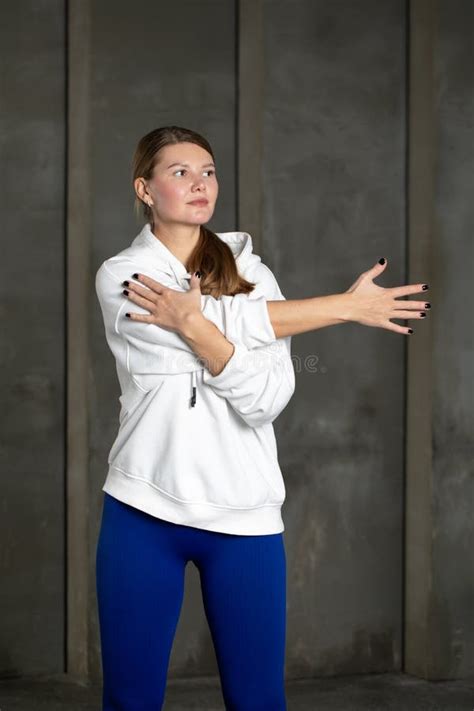 An Athlete in Leggings and a Hoodie Stretches Her Arm, Warming Up the Shoulder Muscles ...