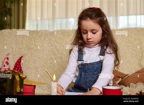 Cute child, a lovely little girl writing a Christmas wish letter to Santa Claus, in a home ...