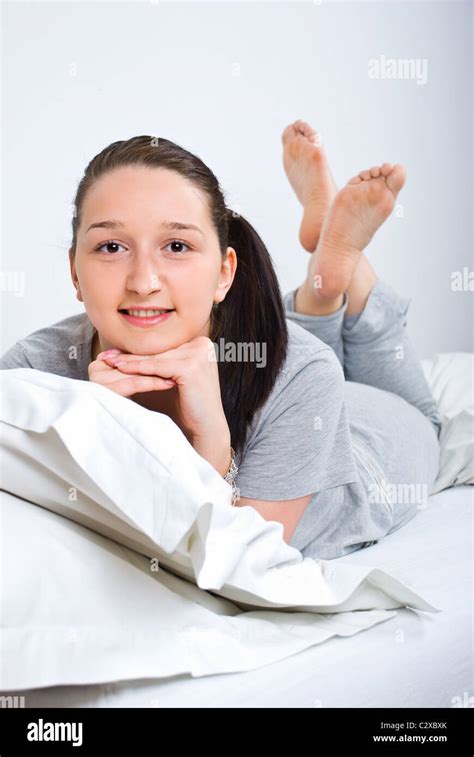 Happy young woman lying down on bed barefoot Stock Photo - Alamy