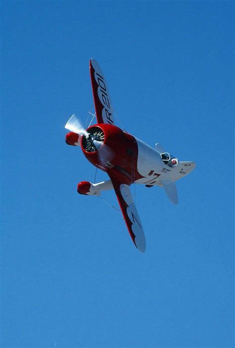 a small red and white plane flying in the sky with it's landing gear down