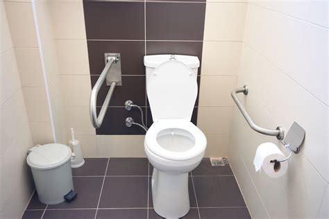 a white toilet sitting in a bathroom next to a trash can and paper towel dispenser