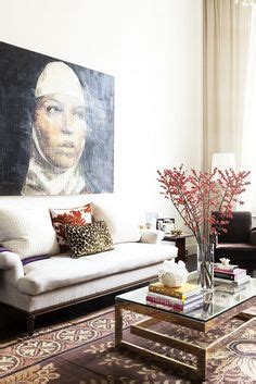 Living room with hung portrait over a white couch, glass coffee table and stacked books. Chic ...